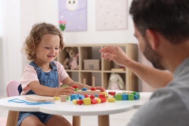 Photo of Motor skills development. Father and daughter playing with stacking and counting game at table indoors