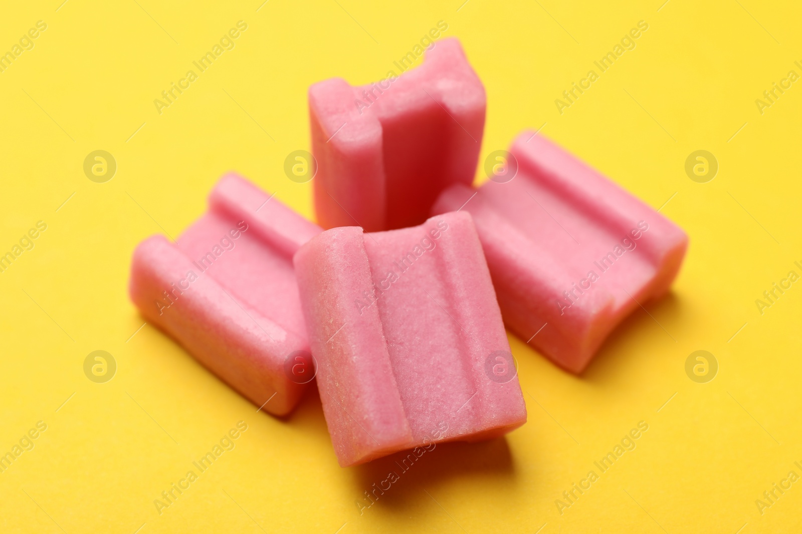 Photo of Tasty pink chewing gums on yellow background, closeup