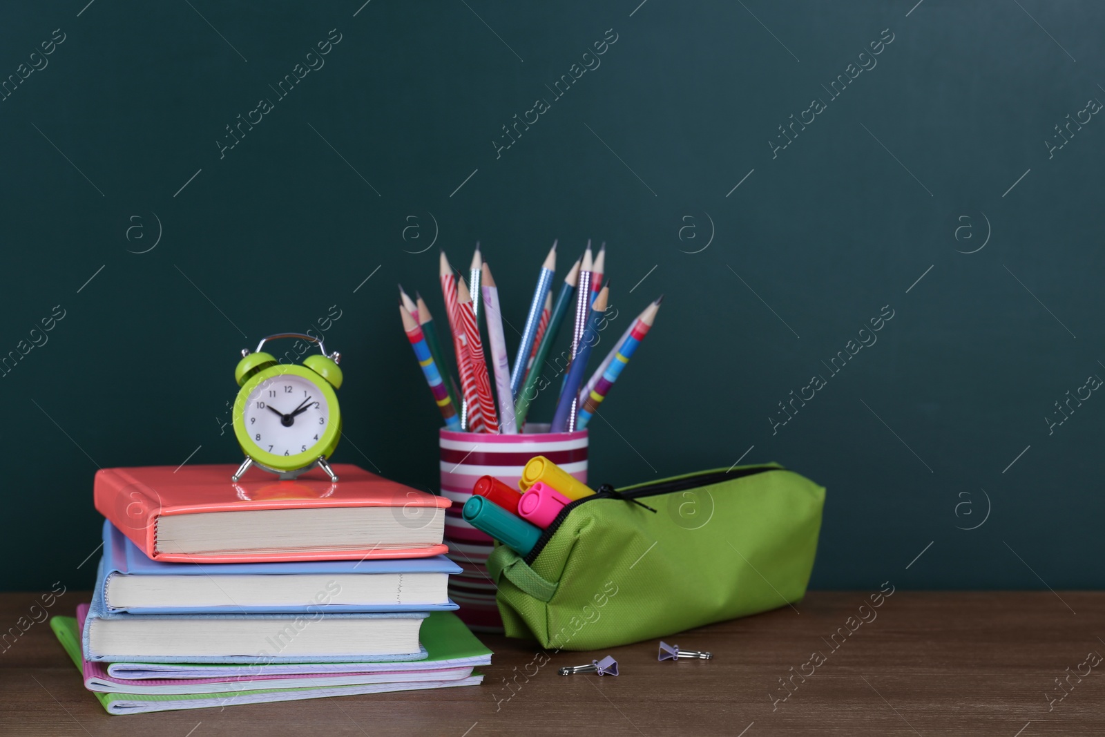Photo of Composition with stationery and alarm clock on table near chalkboard, space for text. Doing homework