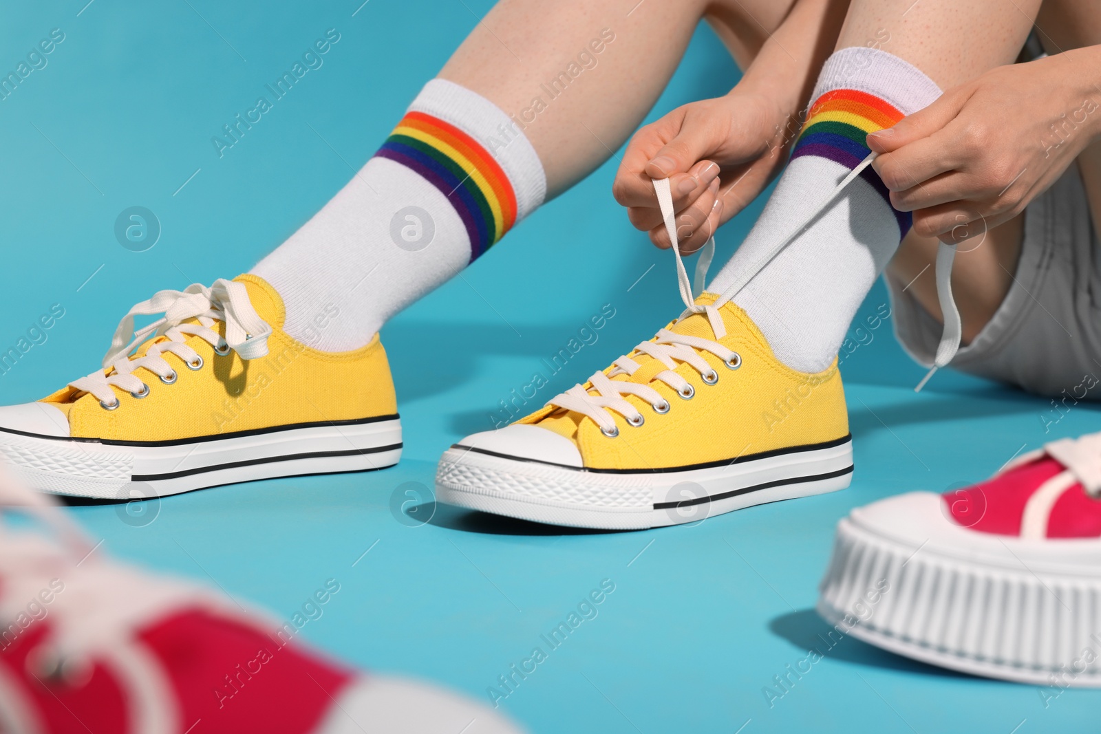 Photo of Woman lacing up yellow classic old school sneakers against light blue background, closeup