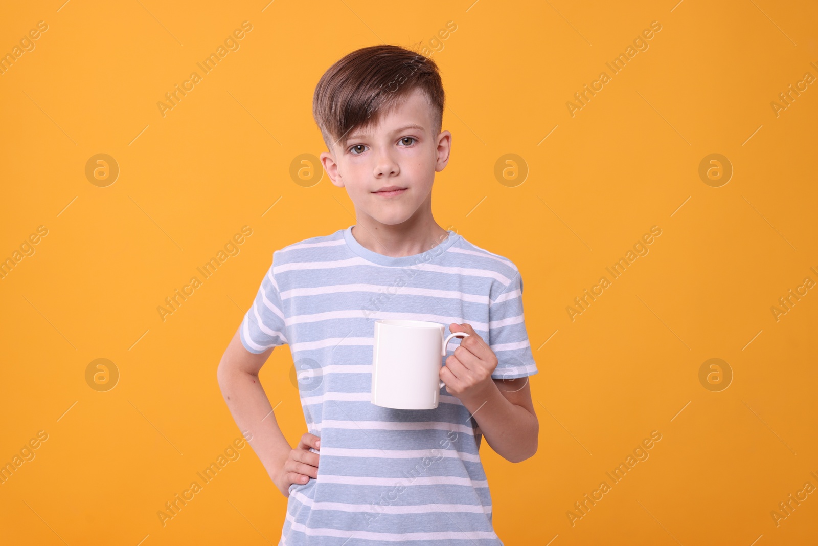 Photo of Cute boy with white ceramic mug on orange background