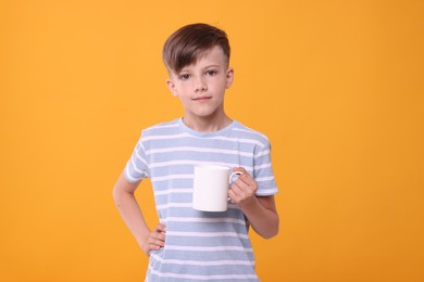 Cute boy with white ceramic mug on orange background