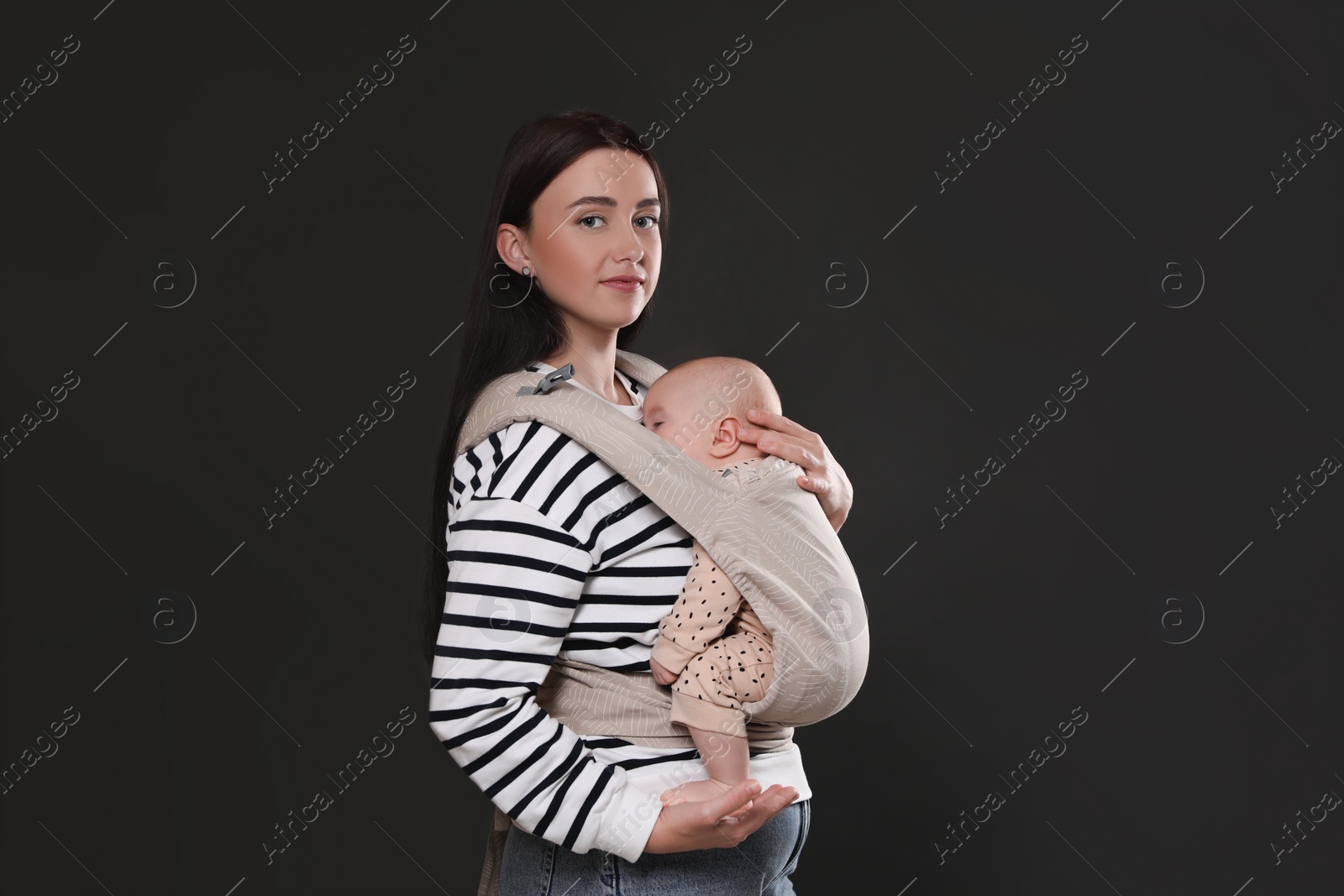 Photo of Mother holding her child in baby carrier on black background. Space for text