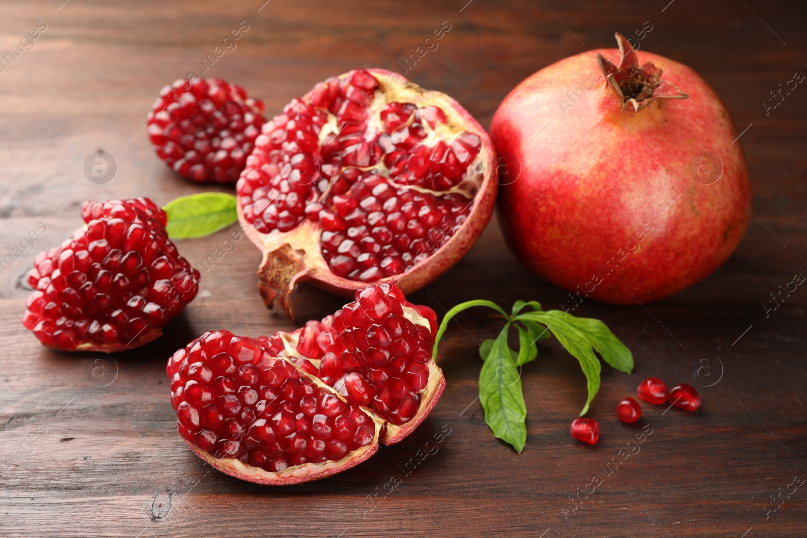 Photo of Fresh pomegranates and green leaves on wooden table