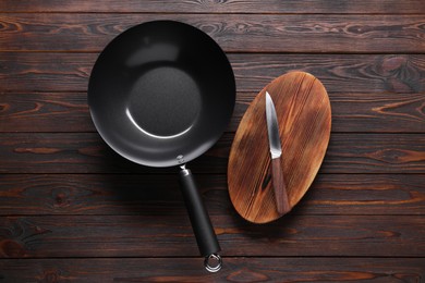 Empty iron wok, knife and cutting board on wooden table, flat lay