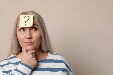 Photo of Emotional mature woman with question mark on beige background. Space for text