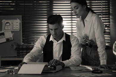 Photo of Old fashioned detective with his colleague working in office. Black and white effect