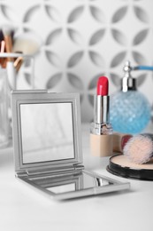 Stylish pocket mirror and cosmetic products on white table