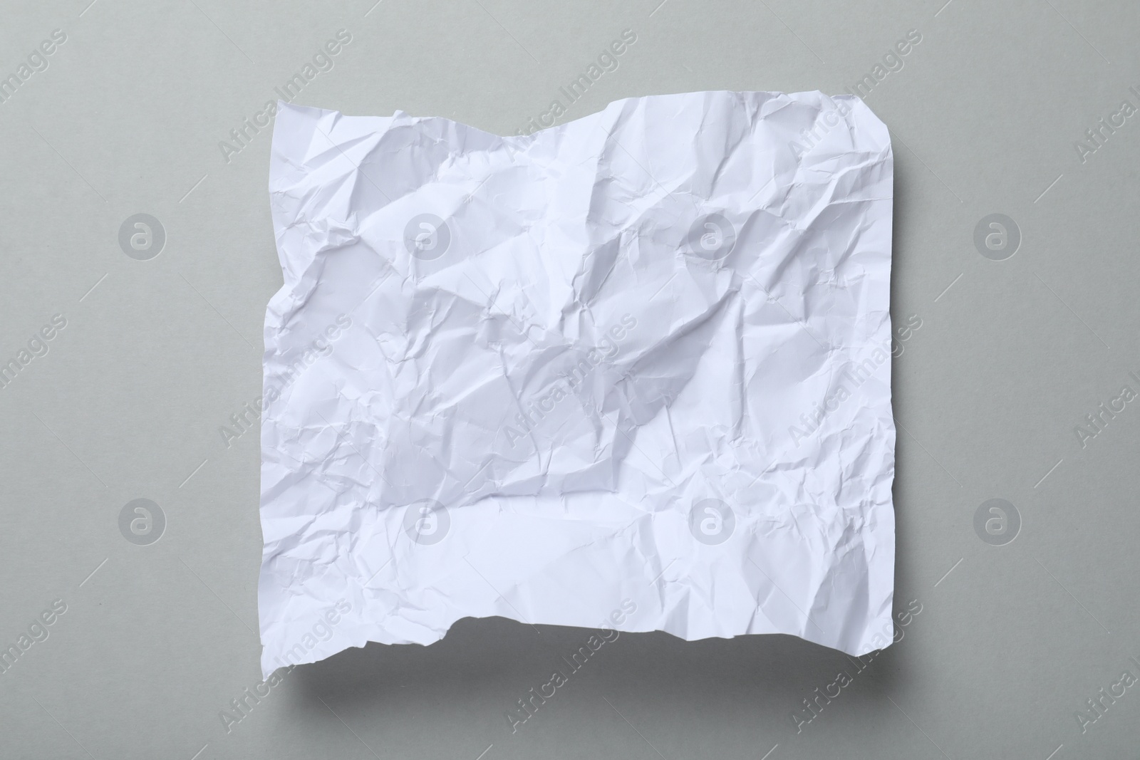 Photo of Sheet of white crumpled paper on grey background, top view