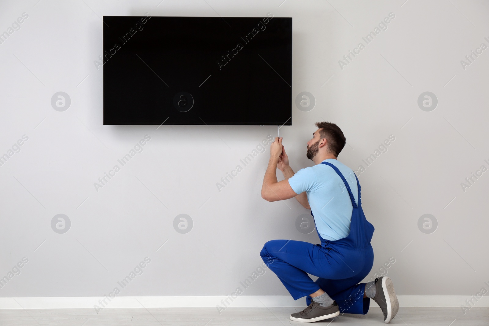 Photo of Professional technician with screwdriver installing modern flat screen TV on wall indoors