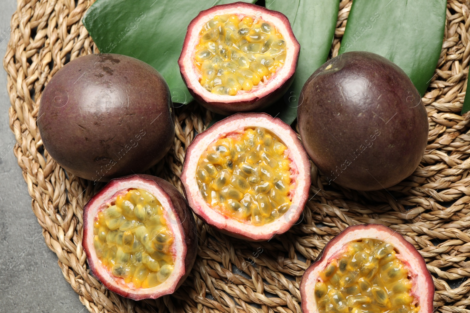 Photo of Passion fruits (maracuyas) and green leaf on wicker mat, flat lay