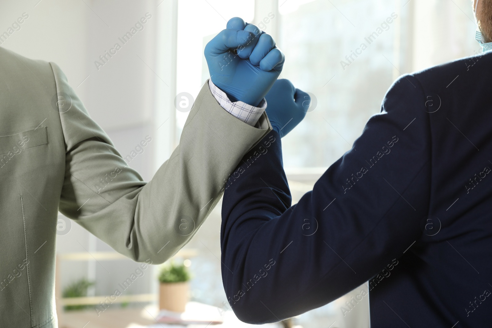 Photo of Office employees greeting each other by bumping elbows at workplace, closeup