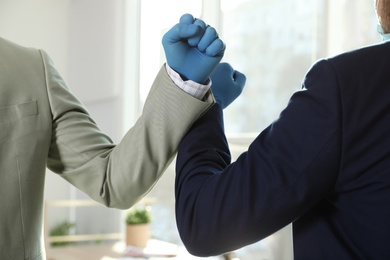 Office employees greeting each other by bumping elbows at workplace, closeup