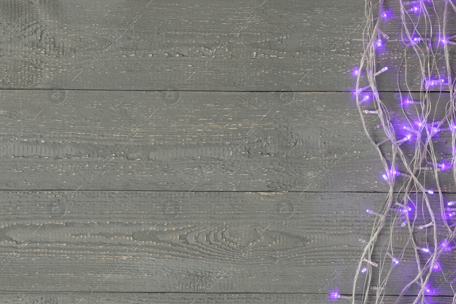 Photo of Glowing Christmas lights on wooden background, top view. Space for text