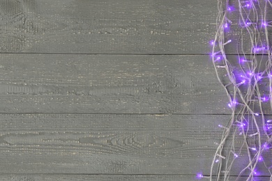 Glowing Christmas lights on wooden background, top view. Space for text