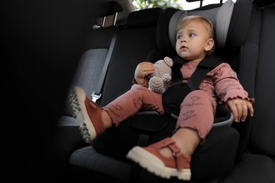 Cute little girl sitting in child safety seat inside car