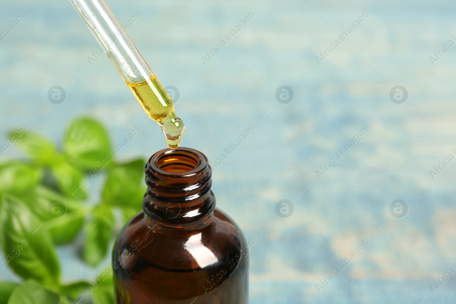 Photo of Dropping basil oil into glass bottle on table. Space for text