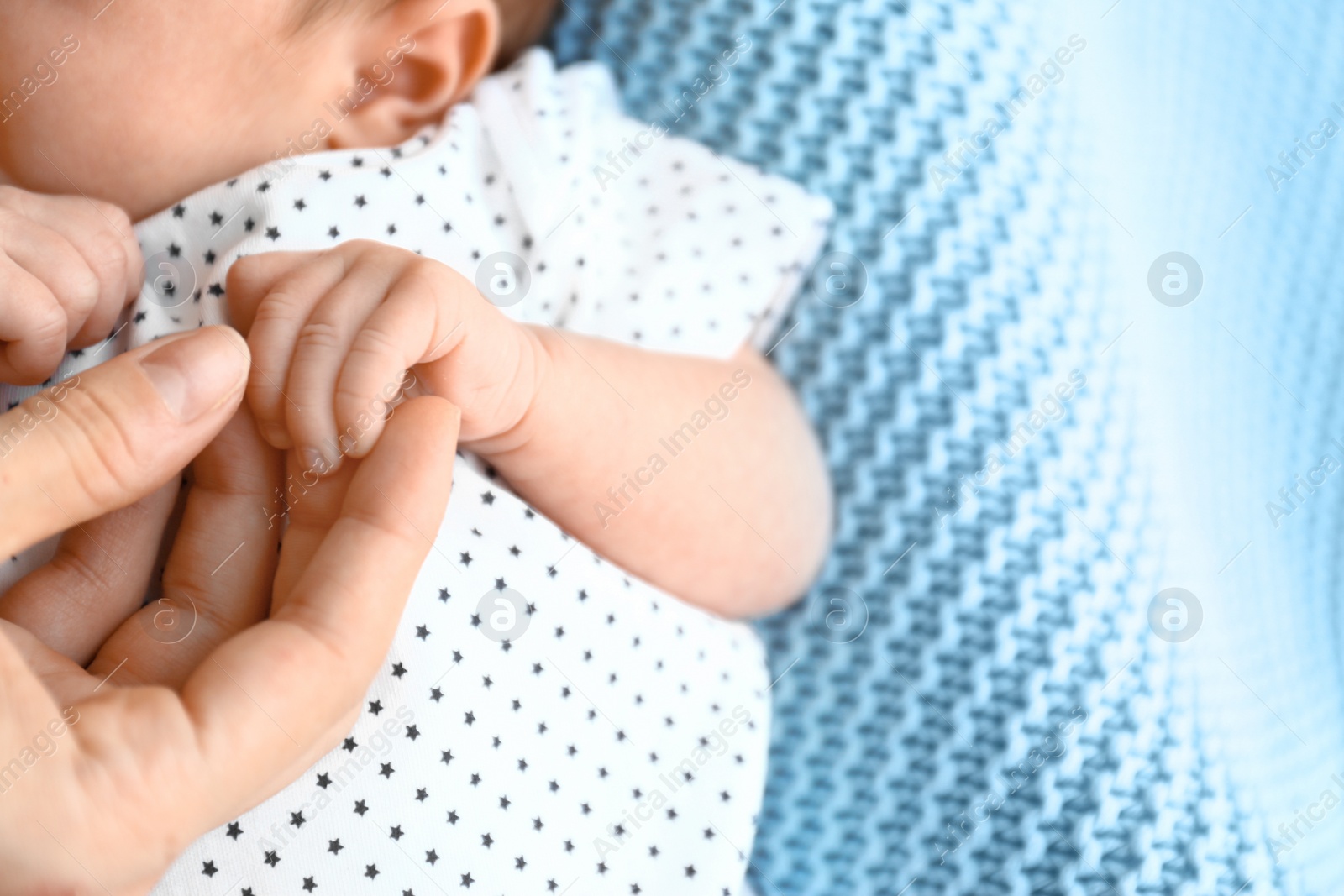 Photo of Cute little baby holding mother's hand on light blue plaid, closeup. Space for text