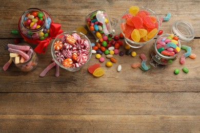 Jars with different delicious candies on wooden table, flat lay. Space for text