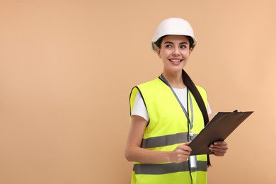 Engineer in hard hat holding clipboard on beige background, space for text