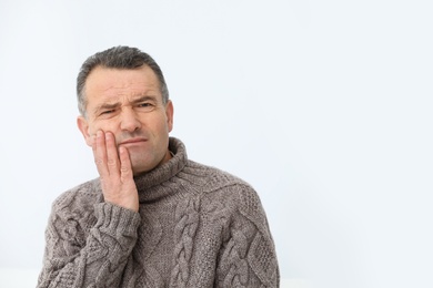 Photo of Mature man suffering from strong tooth pain on light background, space for text