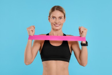 Photo of Woman exercising with elastic resistance band on light blue background