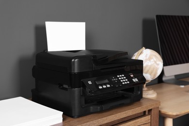 Modern printer with paper near computer on wooden desk at home