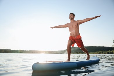 Photo of Man practicing yoga on light blue SUP board on river at sunset