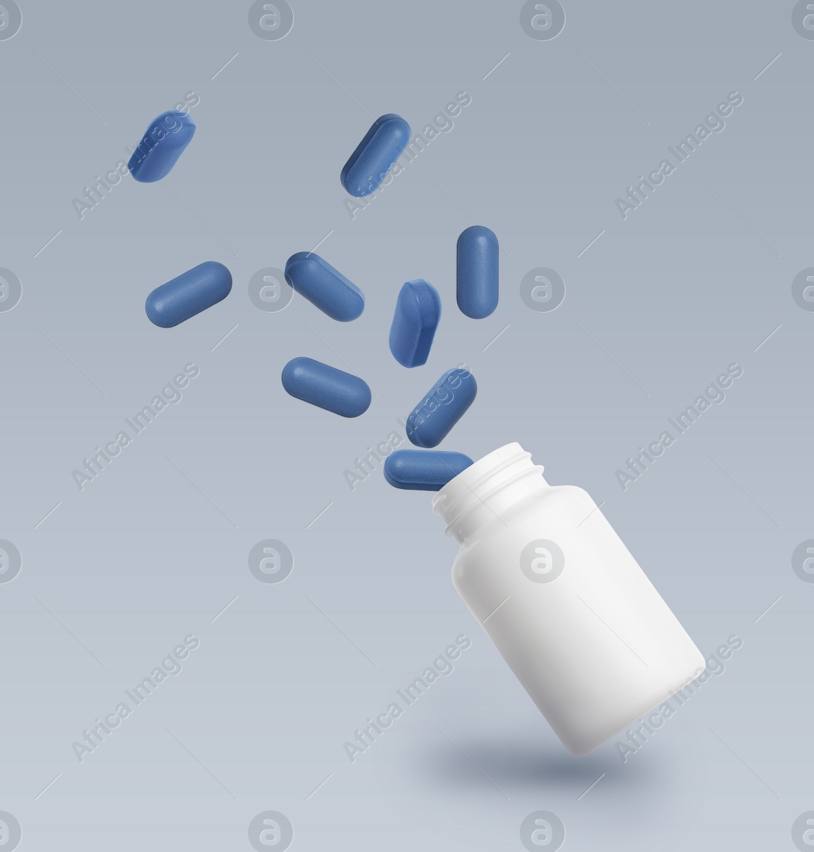 Image of Vitamin pills and bottle in air against grey background