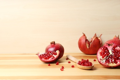 Photo of Composition with ripe pomegranates and spoon of seeds on wooden table, space for text