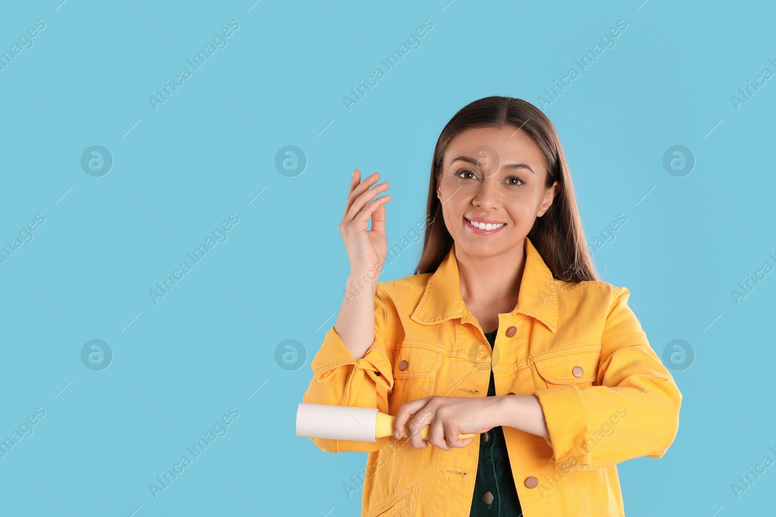 Photo of Young woman cleaning clothes with lint roller on light blue background. Space for text