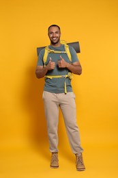 Photo of Happy tourist with backpack showing thumbs up on yellow background