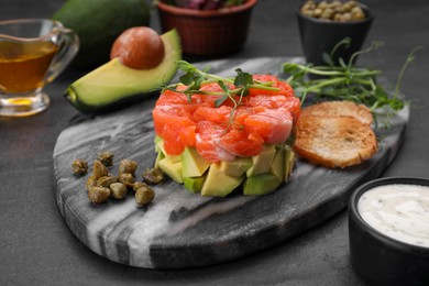 Delicious salmon tartare served with avocado and croutons on dark table, closeup