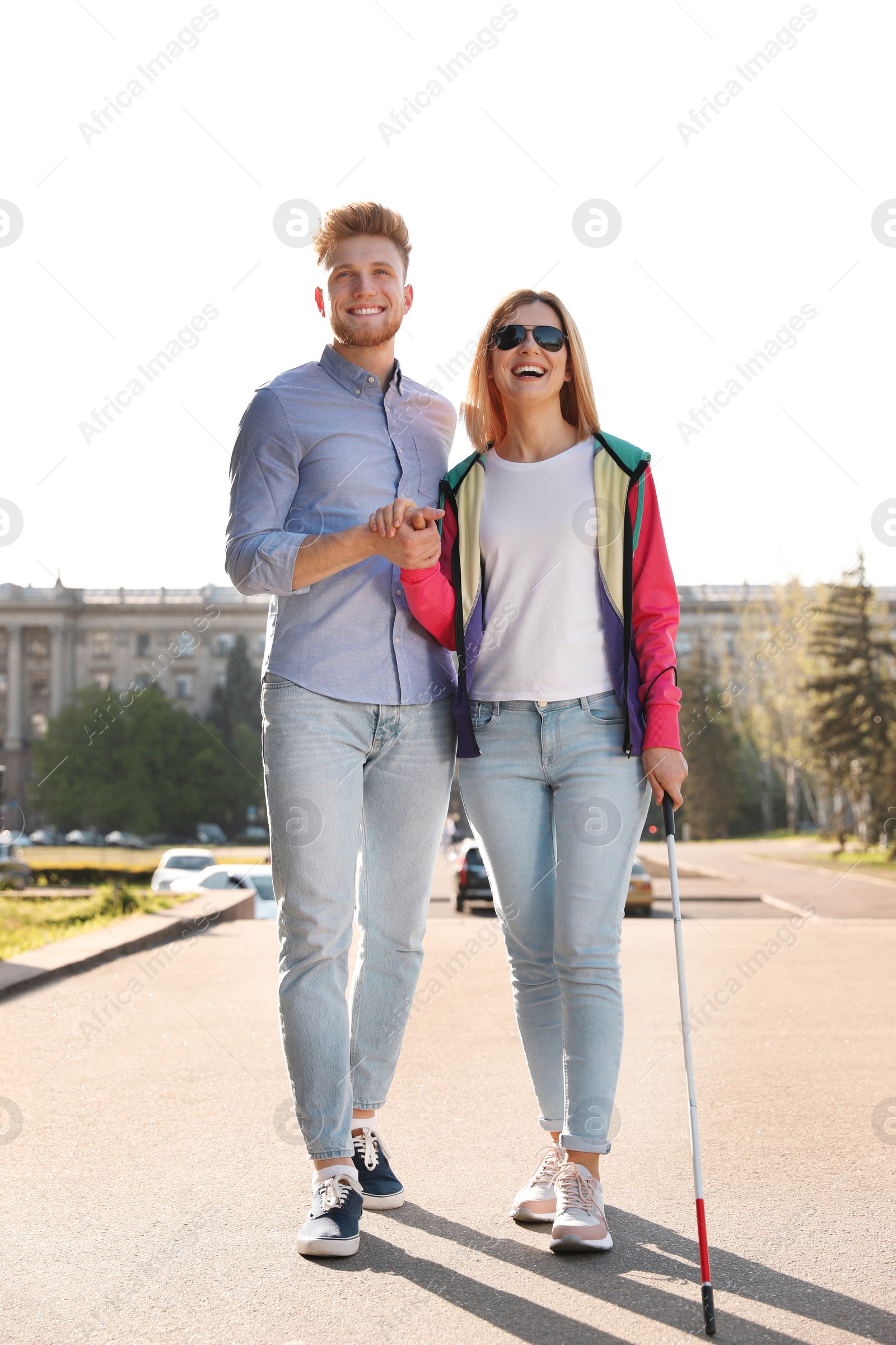 Photo of Young man helping blind person with long cane walking outdoors