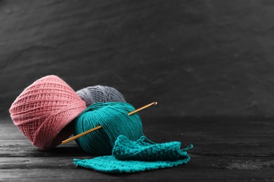Photo of Clews of colorful knitting threads and crochet hook on black wooden table, space for text