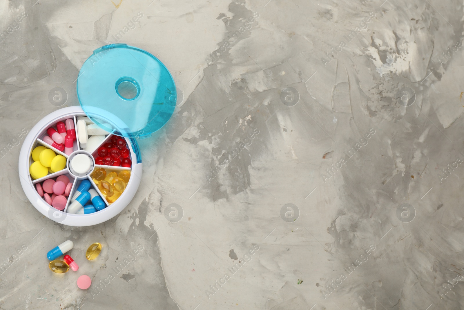 Photo of Plastic box and different pills on light grey stone table, flat lay. Space for text