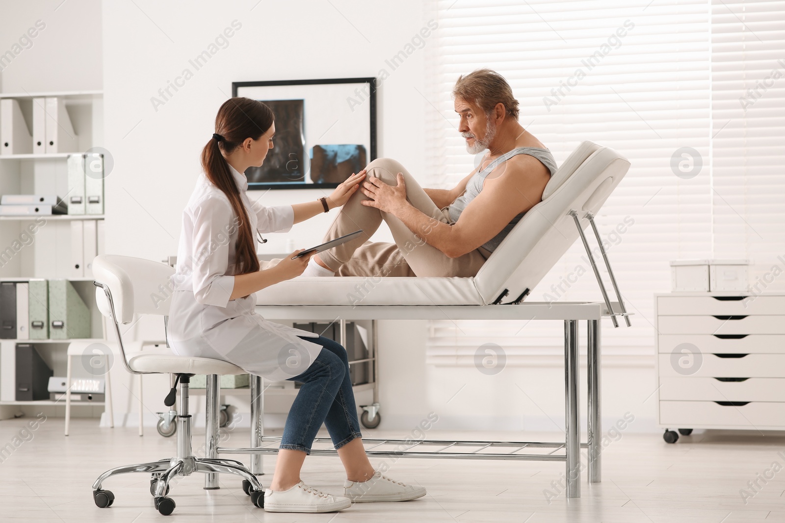 Photo of Orthopedist examining patient with injured knee in clinic