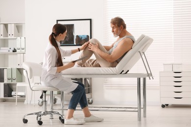 Photo of Orthopedist examining patient with injured knee in clinic