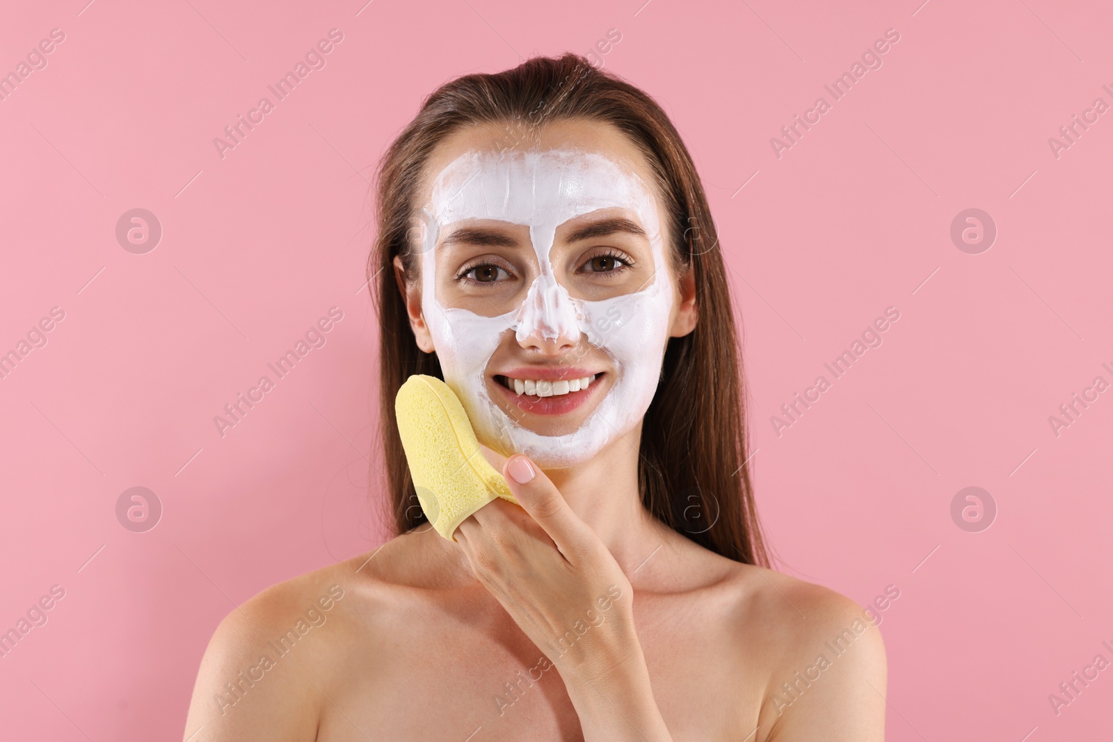 Photo of Happy young woman with face mask and sponge on pink background