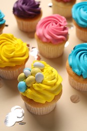 Photo of Delicious cupcakes with bright cream and confetti on beige background, closeup