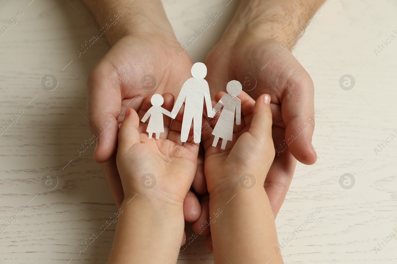 Photo of Father and child holding paper cutout of family at white wooden table, top view