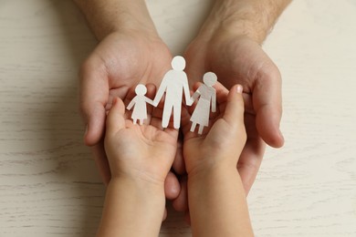 Father and child holding paper cutout of family at white wooden table, top view