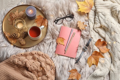 Photo of Flat lay composition with book, cup of tea and warm clothes on fuzzy rug