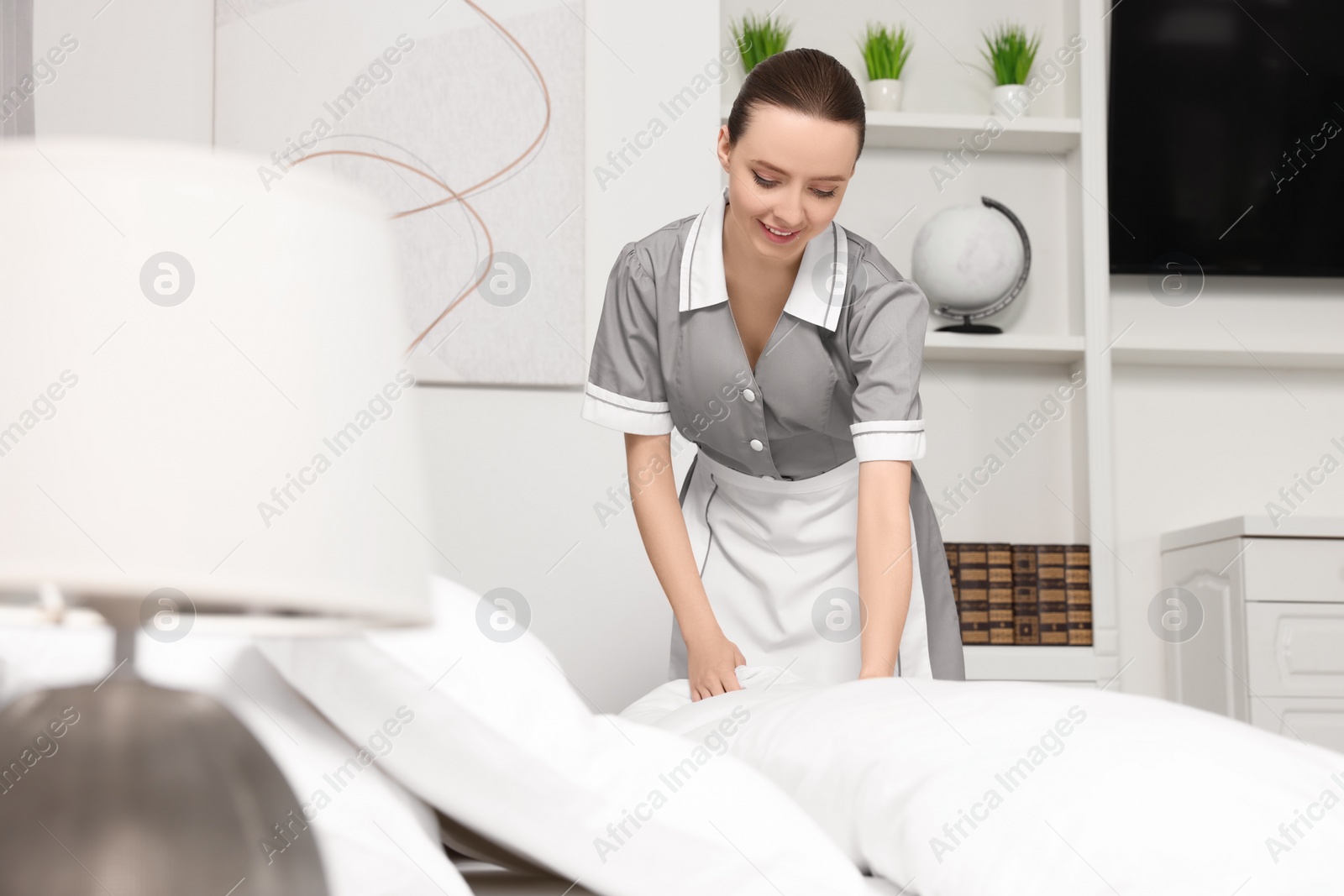 Photo of Young maid making bed in hotel room