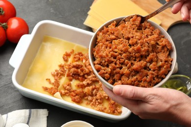 Woman making lasagna at dark table, closeup