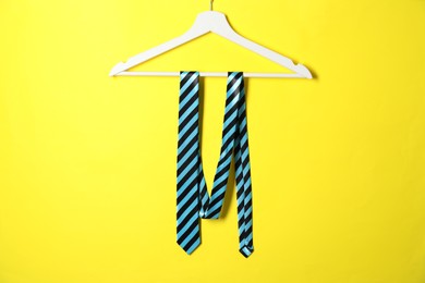 Photo of Hanger with striped necktie on yellow background