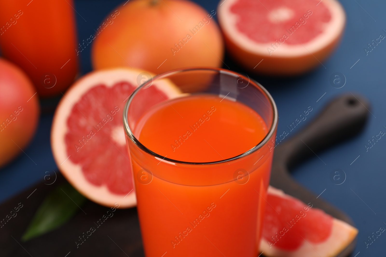Photo of Tasty grapefruit juice in glass and fresh fruits on blue table, closeup