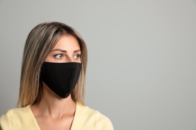 Photo of Young woman in protective face mask on light grey background. Space for text