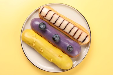 Photo of Delicious eclairs covered with glaze on yellow background, top view