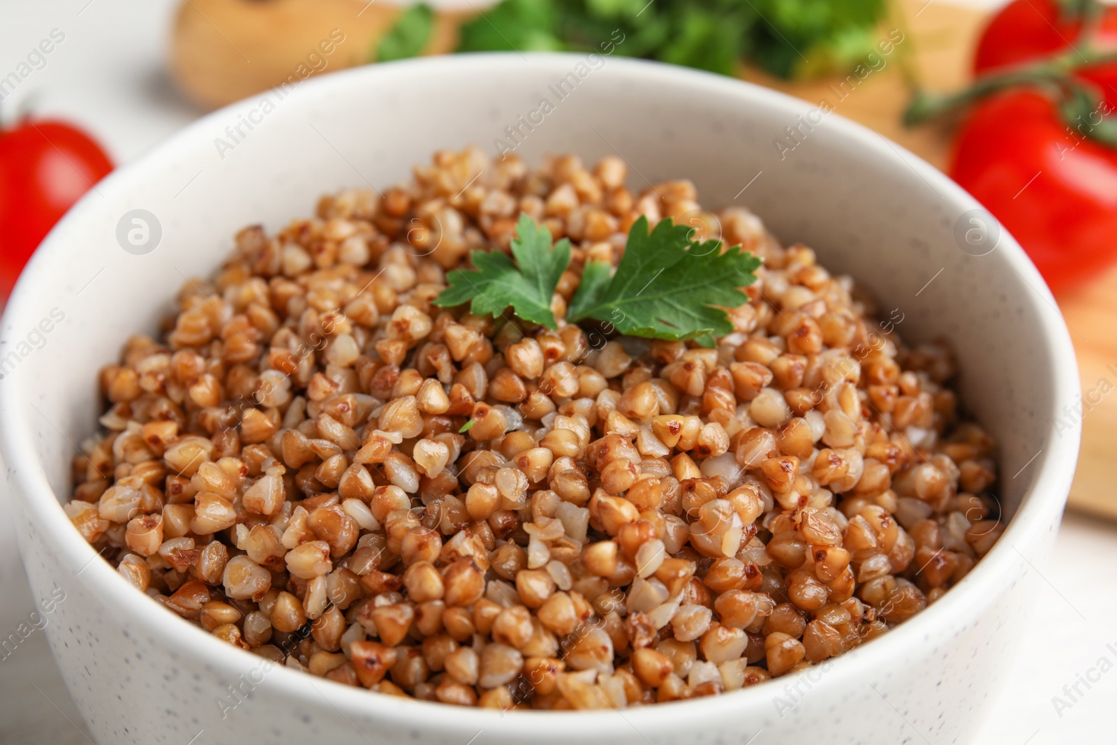 Photo of Bowl of buckwheat porridge with parsley on table, closeup